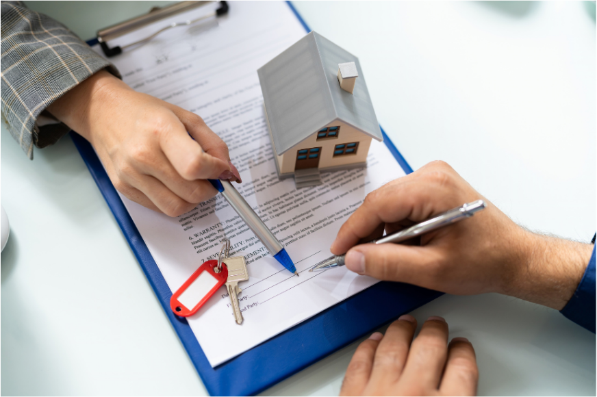 Pessoa assinando documento imobiliário, com chave e miniatura de casa sobre a mesa, representando o registro da partilha de inventário.